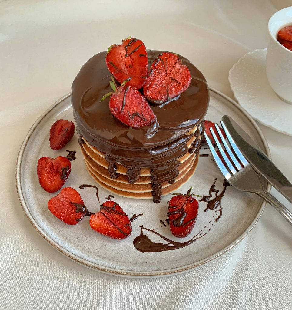 A tempting stack of pancakes topped with chocolate syrup and fresh strawberries.
